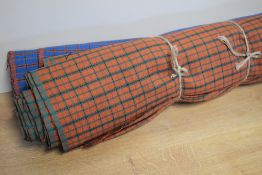 Two bolts of fine wool tartan fabric, one mostly blue with orange/red and black check, the other