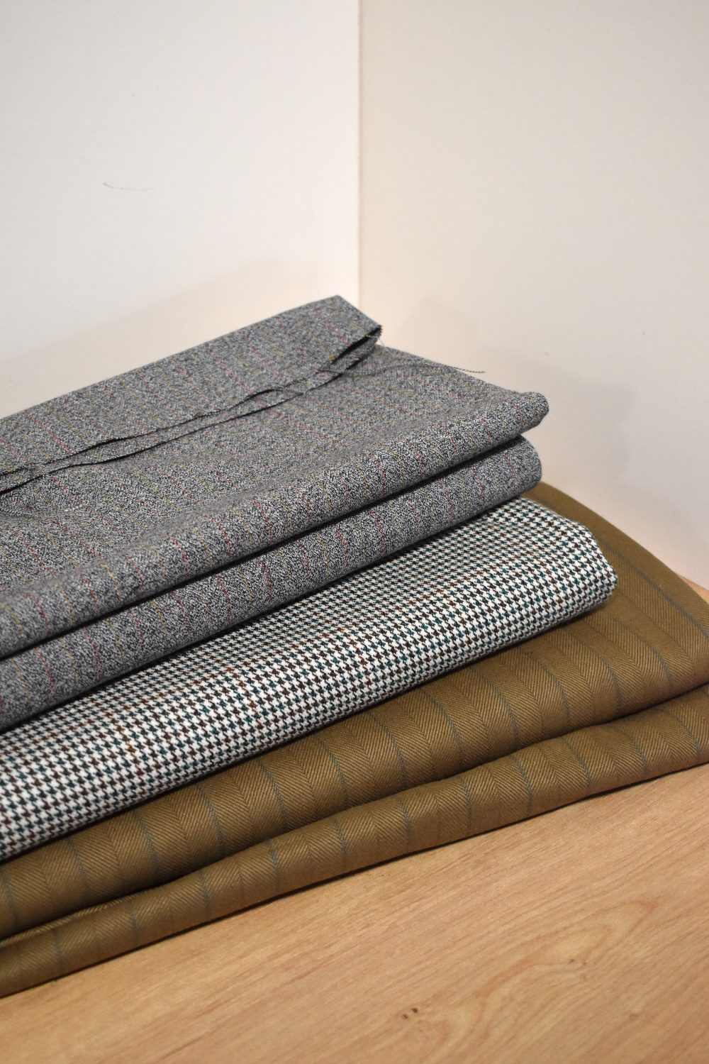 Three bolts of vintage tailor's fabric, including a wool houndstooth in teal and brown, a grey