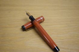 A Parker Duofold Junior button fill fountain pen in orange with two gold bands to the cap having