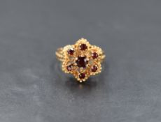 A yellow metal garnet cluster ring, the central round cut garnet with a six garnet surround in a