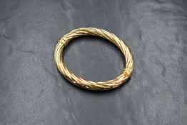 A 9ct gold hinged bangle, of twisted form with safety clip, approximately 6cm internal diameter,