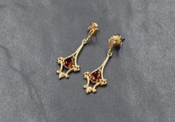 A pair of 9ct gold garnet drop earrings, the pear cut garnets in decorative pierced scroll motif