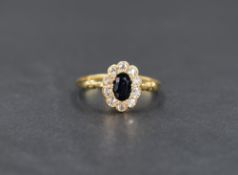 A yellow metal (presumed gold) sapphire and diamond cluster ring, the central oval cut blue sapphire