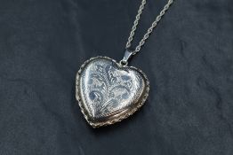 A large silver heart shaped locket, having engraved scroll decoration and twist thread, on a