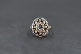 A yellow metal and paste set cluster ring, the central oval cut blue paste having a clear paste