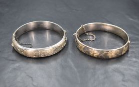 Two silver hinged bangles, one having decorative scroll engraving and the other with a textured leaf