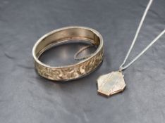 A silver hinged bangle, having engraved floral and scroll decoration with safety chain, along with a