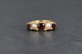 A yellow metal (presumed gold) garnet and pearl five stone ring, the central round cut garnet