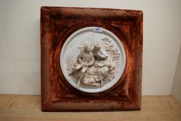 A circular cast plaster wall relief depicting a romantic scene of lovers, mounted in a red velvet