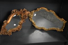 A pair of ornate vintage wall mirrors decorated having gilt frames with classical motifs, largest