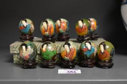A set of 10 miniature green stone eggs hand painted with female figures on a carved wooden base,