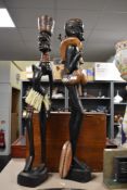 A pair of tall carved African tribal sculptures depicting a male hunter carrying a deer and female