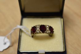 A yellow metal three stone ring, the three graduated oval cut red paste interspersed with four clear