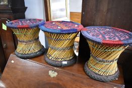 A set of three ethnic art style stools or occasional tables having woolwork tops with woven frames