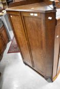 An early 20th Century oak corner cupboard having ledge back, panel doors and turned feet, height