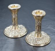 A pair of Elizabeth II silver candlesticks, having embossed decoration and step moulding to the