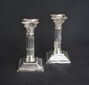A pair of George V silver Corinthian column candlesticks, having concave square detachable sconces