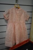 A 1950s early-years childrens dress in baby pink Bri-Nylon, comprising two dresses to be worn