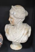 A large terracotta female bust of classical form supported on a circular base, heavily weathered,