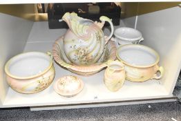 An early 20th century porcelain pitcher and wash basin, decorated with pink and green foliage on a