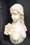 A large resin female bust in cream colour, her hair over one shoulder and a flower on her other,