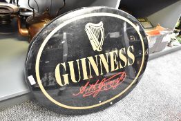 A oval Guinness advertising sign having gold coloured lettering on a black ground, w61cm