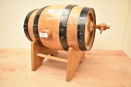 A coopered oak spirit barrel with black painted coopers, wooden spiggot and stand 34.5cm overall.