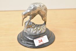 A cast white metal Kiwi bird sculpture supported on a circular wooden base, h10.5cm