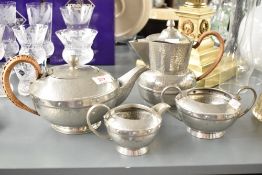 An early 20th century G.M.B pewter tea service having wicker handles and hand beaten decoration,