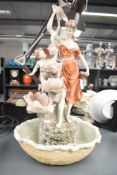 A continental style resin water figure depicting woman and cherub with urn among a flowery