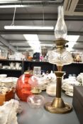 An early 20th century brass oil lamp with glass chimney and red shade, having arts and craft