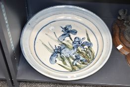 A large and decorative art pottery stoneware charger, decorated with iris flowers within blue