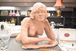 An attractive terracotta sculpture of a nude female figure, crouching with her left hand resting