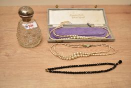 A silver capped cut glass scent bottle, having cherub decoration, along with two rows of faux pearls