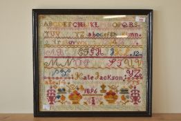 A framed cross stitch sampler, by Kate Jackson aged 14, dated 1896, worked mostly in reds,