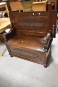 An early 20th Century oak monks bench having figural carved arms and vine applique decoraion,