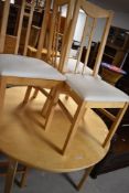 A modern beech effect circular dining table with extension leaves, and four similar dining chairs