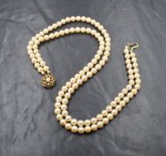 A double string of cultured pearls of even form having a large 9ct gold decorative circular fish