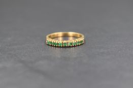 An 18ct gold emerald half eternity band, the nine claw set round cut emeralds, on a yellow metal