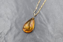 A large teardrop amber pendant, having a silver pin attachment on a 9ct gold curb link chain, marked