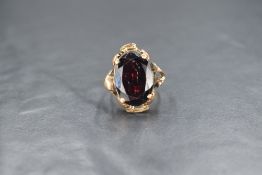 A yellow metal presumed gold garnet set ring, the large oval cut garnet in a four claw setting in