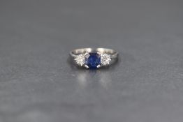 A white metal sapphire and diamond set trilogy ring, ring central emerald cut blue sapphire