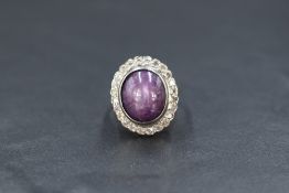 A yellow metal oval star ruby and diamond set ring, the ruby cabochon bearing a subtle asterism in a