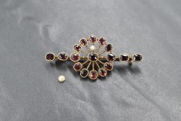 A yellow metal bar brooch stamped 9ct, having a decorative garnet and split seed pearl set