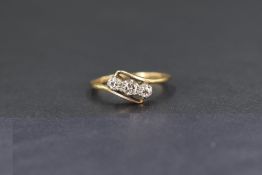 A yellow metal three stone diamond cross over ring, the three small diamonds each measuring