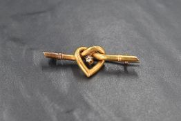 A yellow metal knotted heart bar brooch having a small central diamond, measuring approximately 0.