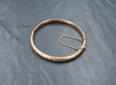 A 9ct gold hinged bangle, having decorative engraving to one side with safety chain, marked 375,