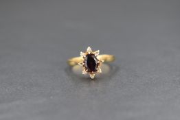 An 18ct gold garnet and diamond set cluster ring, the central oval cut garnet in an eight diamond