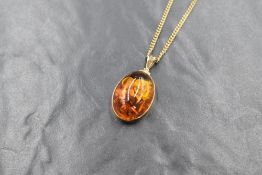 An oval Baltic amber cabochon pendant in a 9ct gold mount with 9ct gold chain, marked 375,