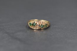 A 9ct gold emerald and diamond ring, the four round cut emeralds with six diamond chips in a pierced